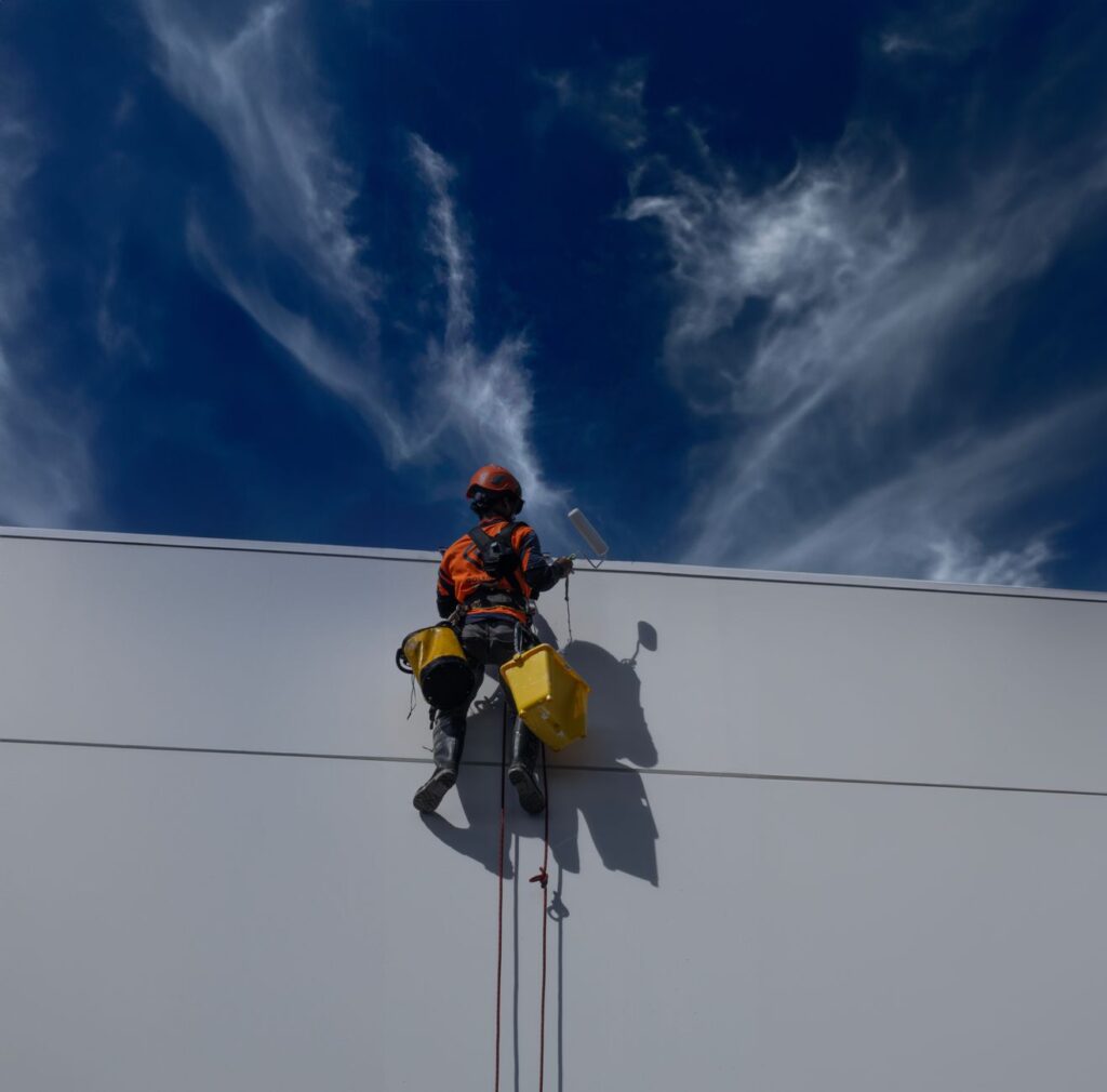 Rope-access painter working on a tall white commercial wall