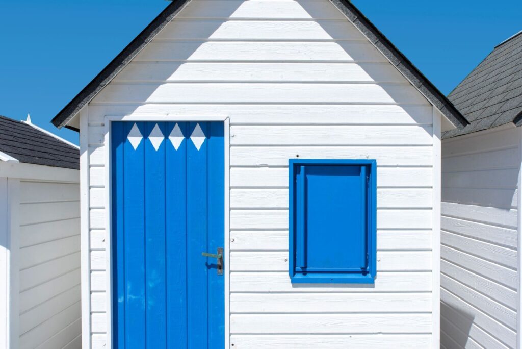 White weatherboard beach cottage with a bright blue door and shutter