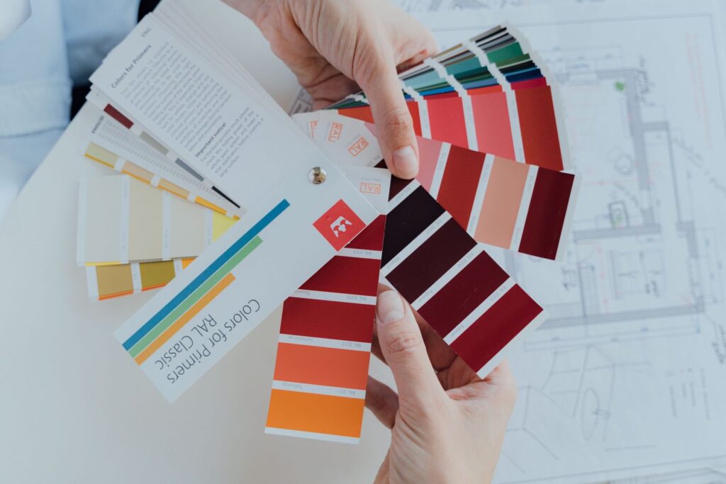 Hands holding a fan of paint colour swatches over plans