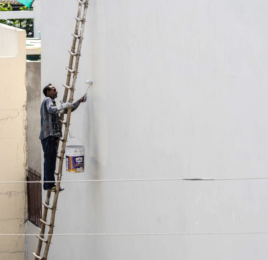 Painter on a ladder painting a white exterior wall