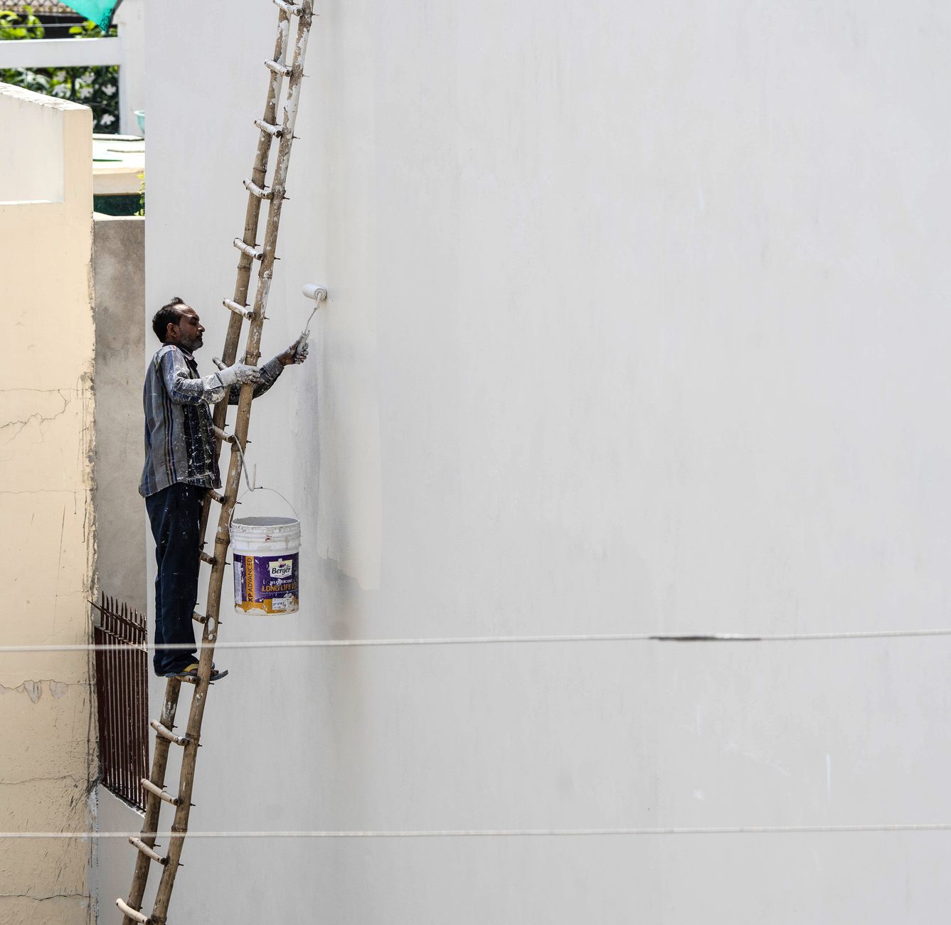 Painter on a ladder painting a white exterior wall