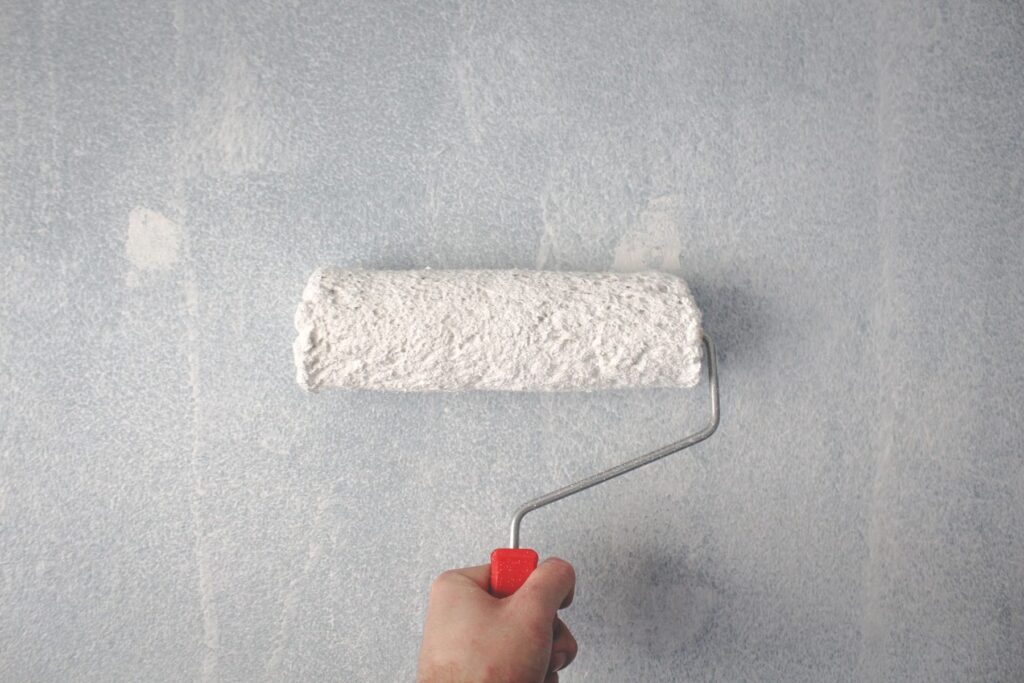A roller loaded with white paint against a freshly painted wall