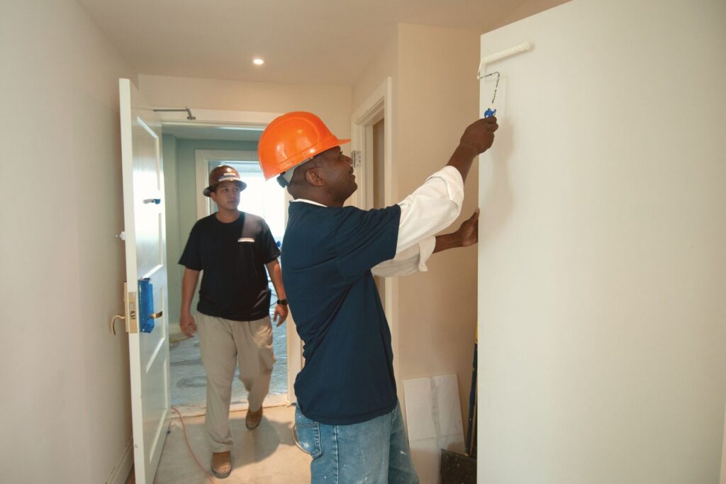 Painter in a hard hat rolling a wall while a colleague checks the work